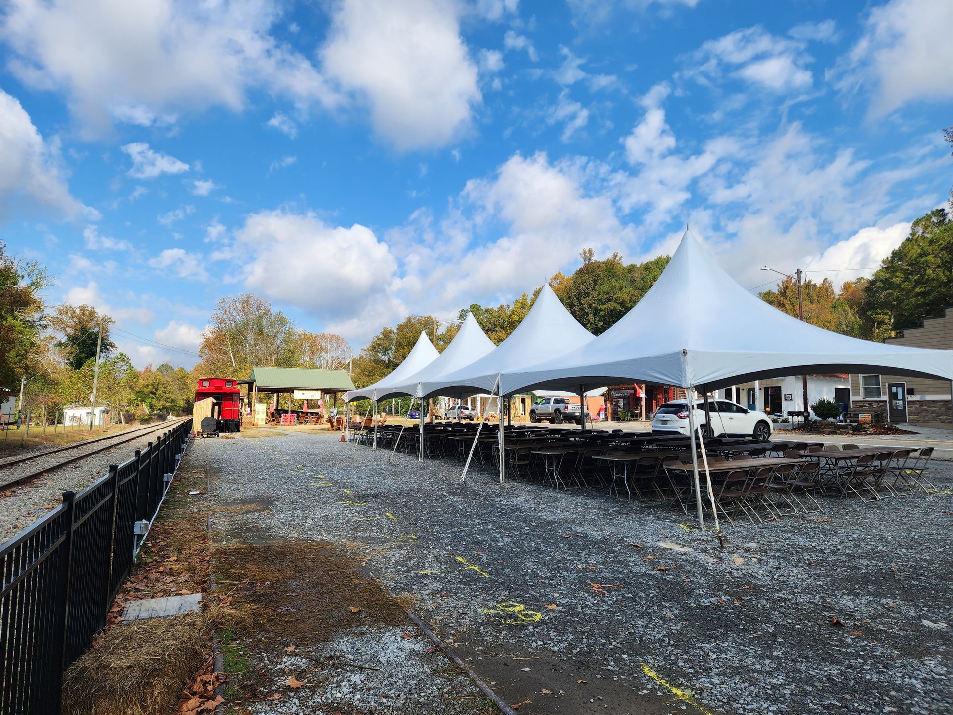 A row of white tents are sitting on top of a gravel lot next to a train track.