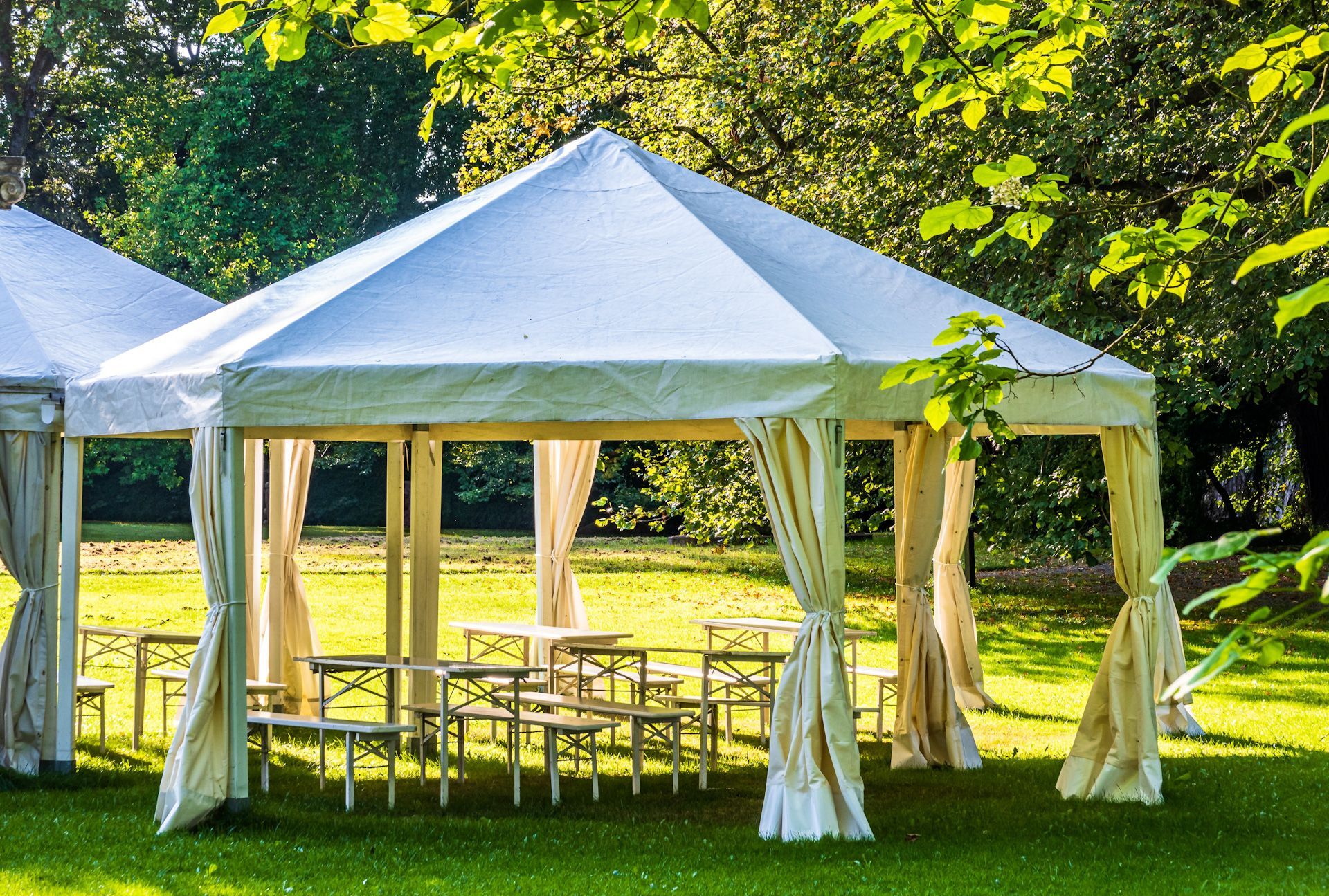 A white tent with tables and chairs in a park