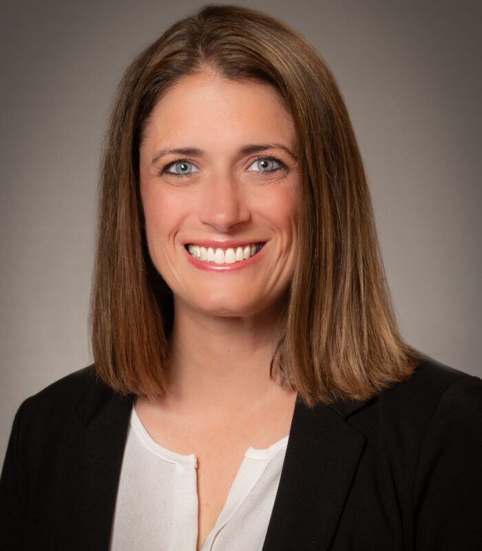 A woman wearing a black sweater and a white shirt is smiling for the camera.