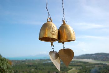 Gold wind chimes blowing in the wind with mountains and an ocean behind them