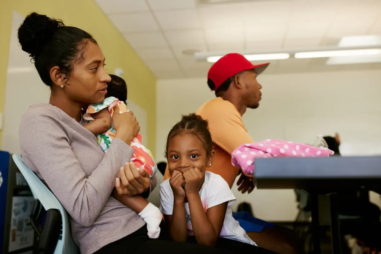 A woman is holding a baby and a little girl is sitting at a table.