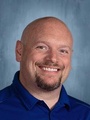 A bald man with a beard is wearing a blue shirt and smiling for the camera.