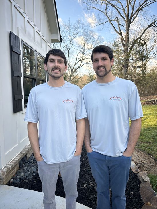 Two men are standing next to each other in front of a house.