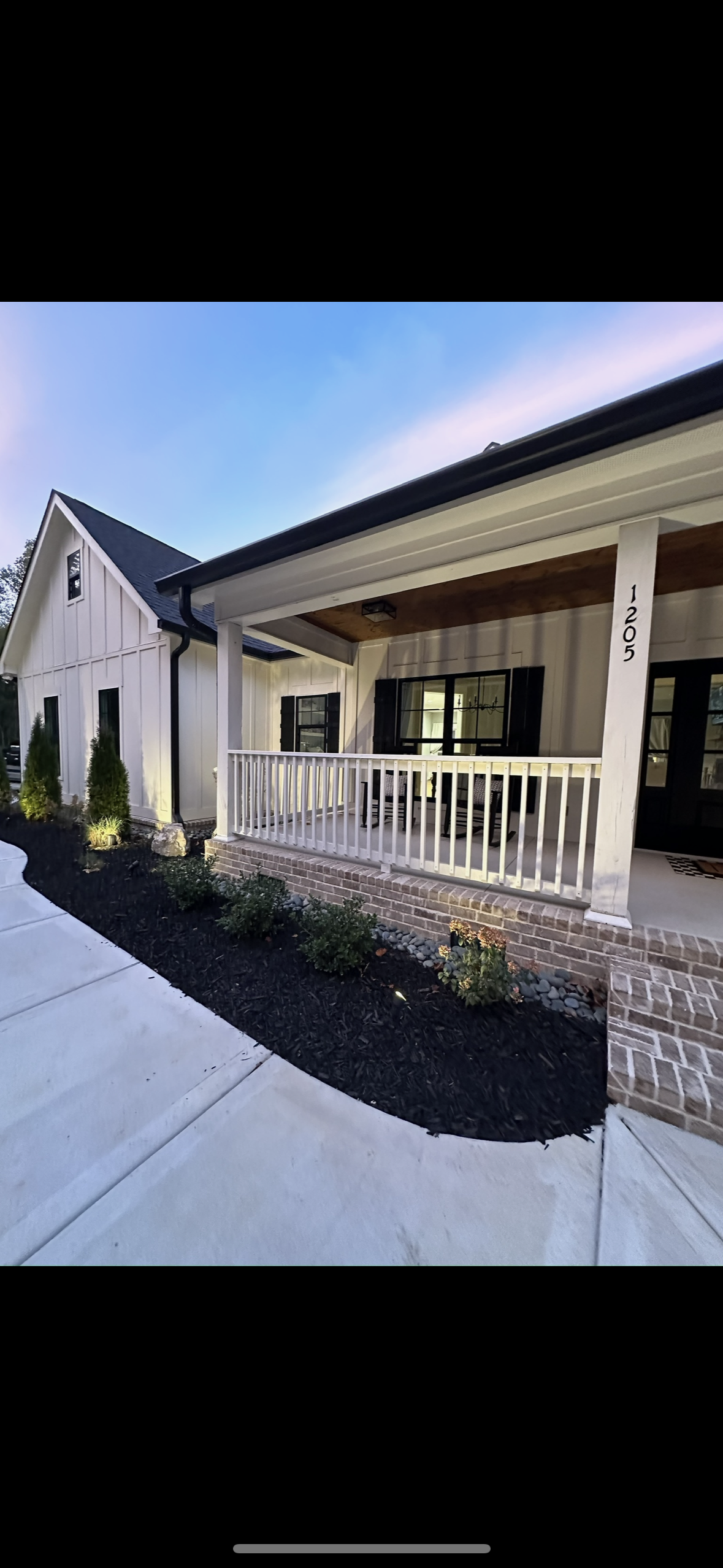 A white house with a large porch and a black roof.