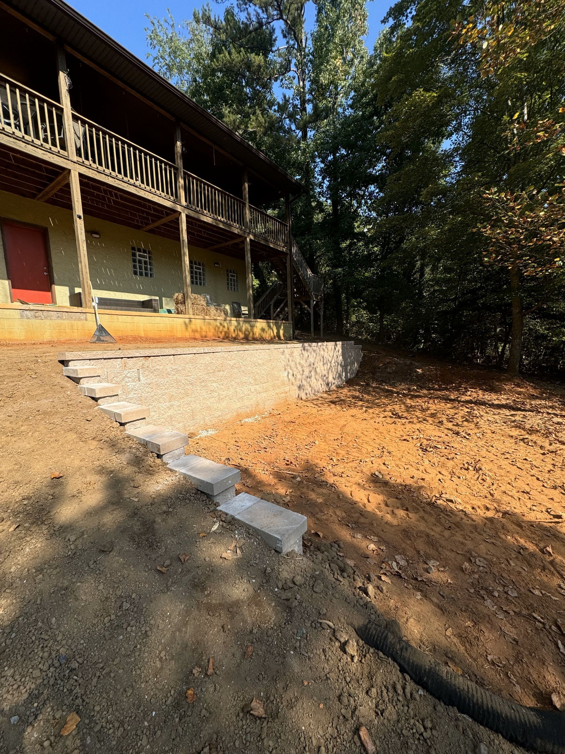 A large house is sitting on top of a dirt hill surrounded by trees.