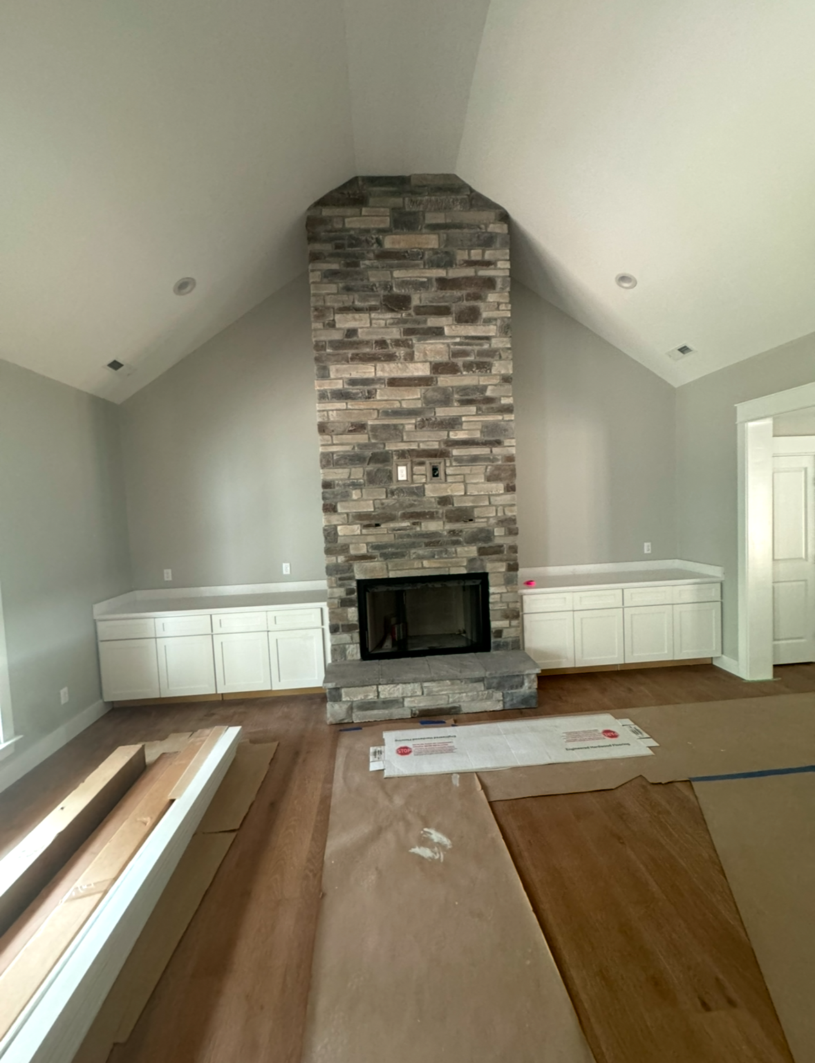 A living room with a stone fireplace and white cabinets.