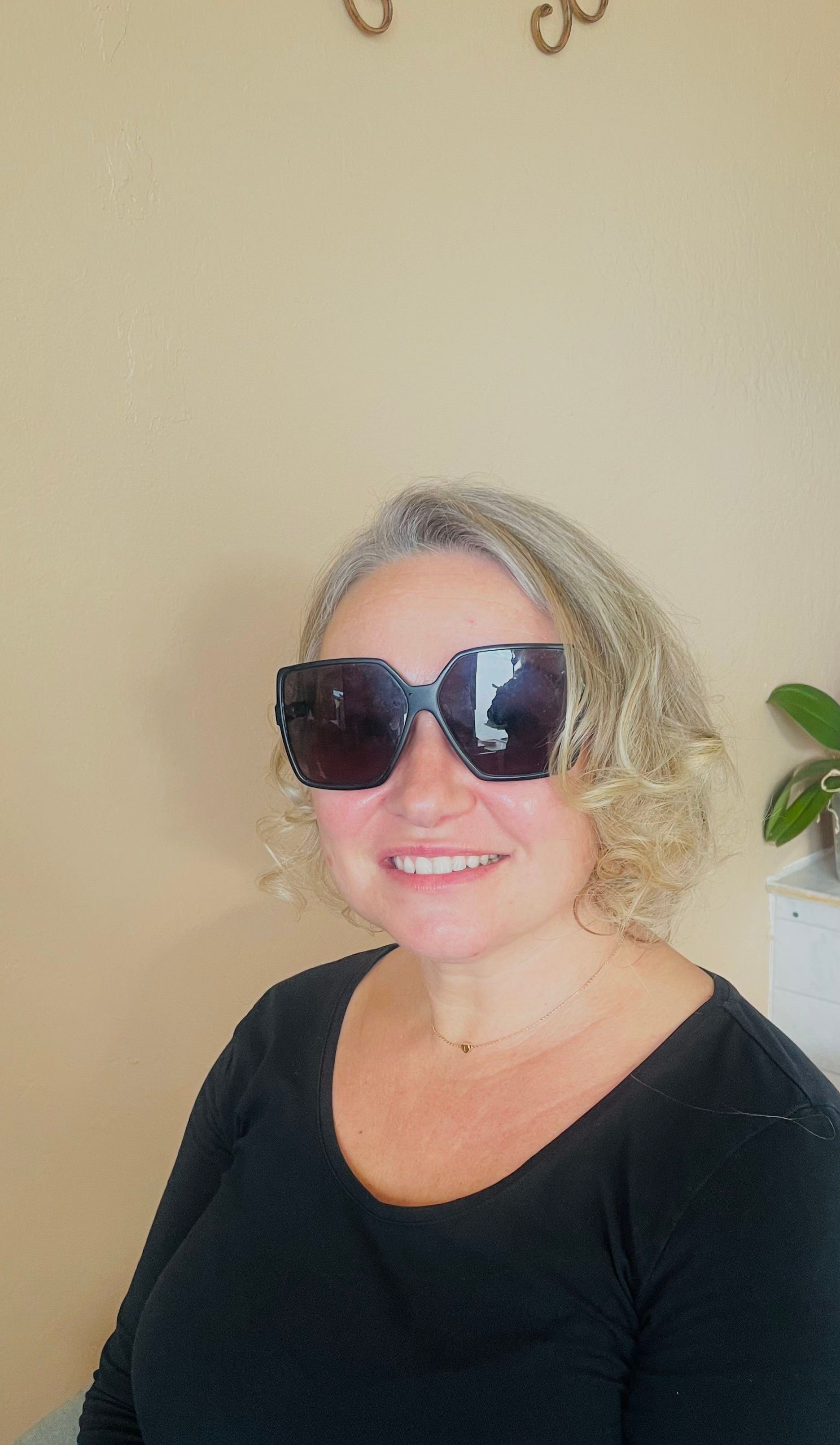 a woman wearing sunglasses and a black shirt is smiling .