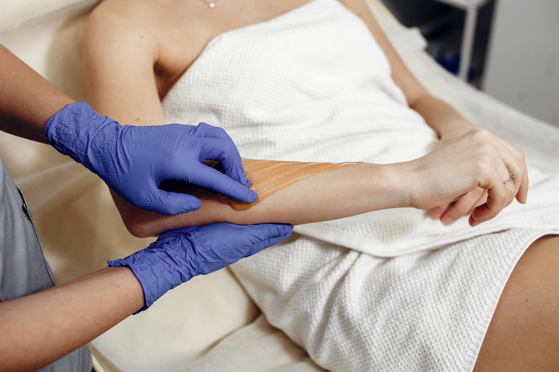 a woman is getting her arm waxed by a woman wearing blue gloves .