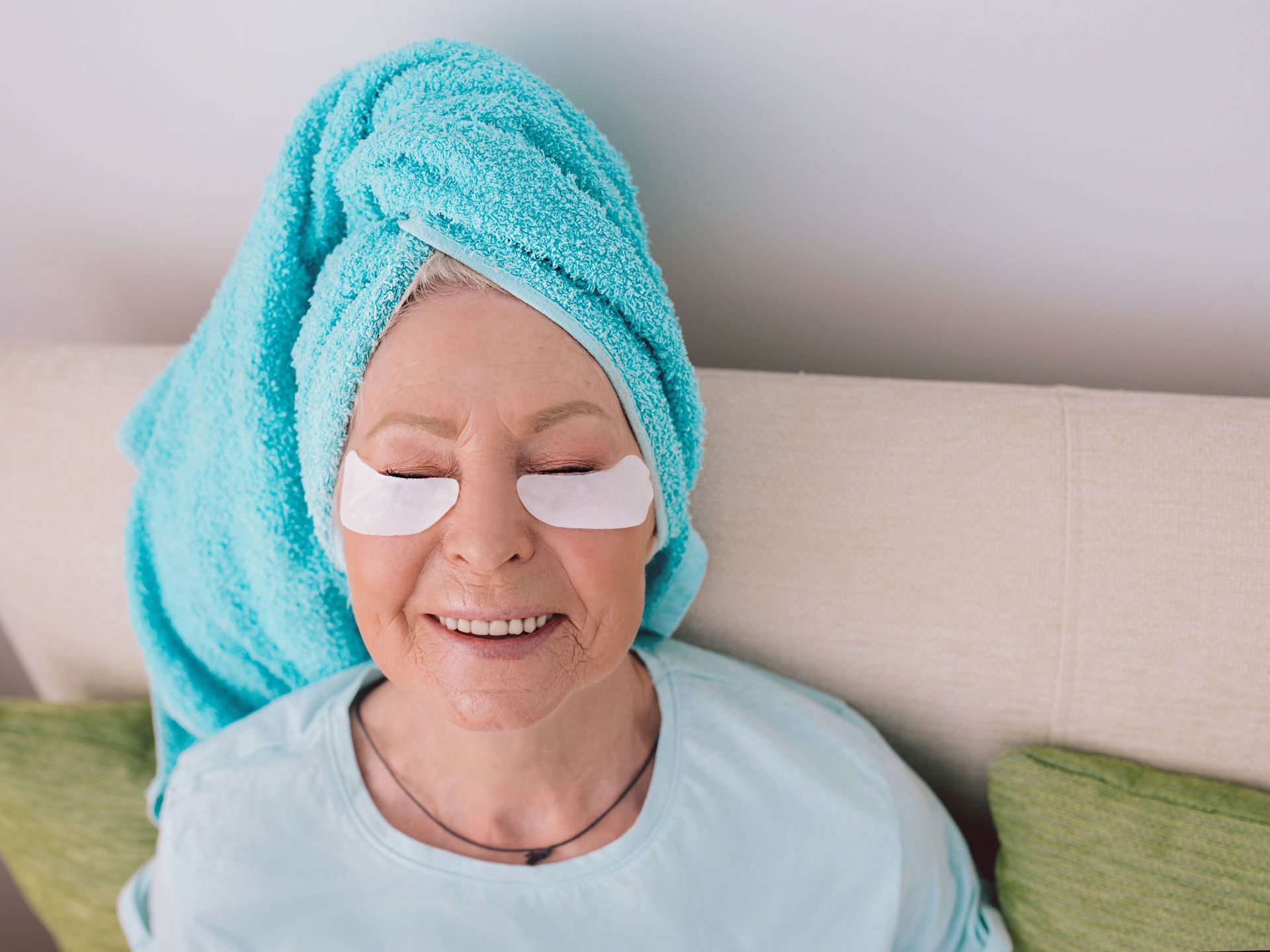 an elderly woman is laying on a couch with a towel wrapped around her head and eye patches on her eyes .