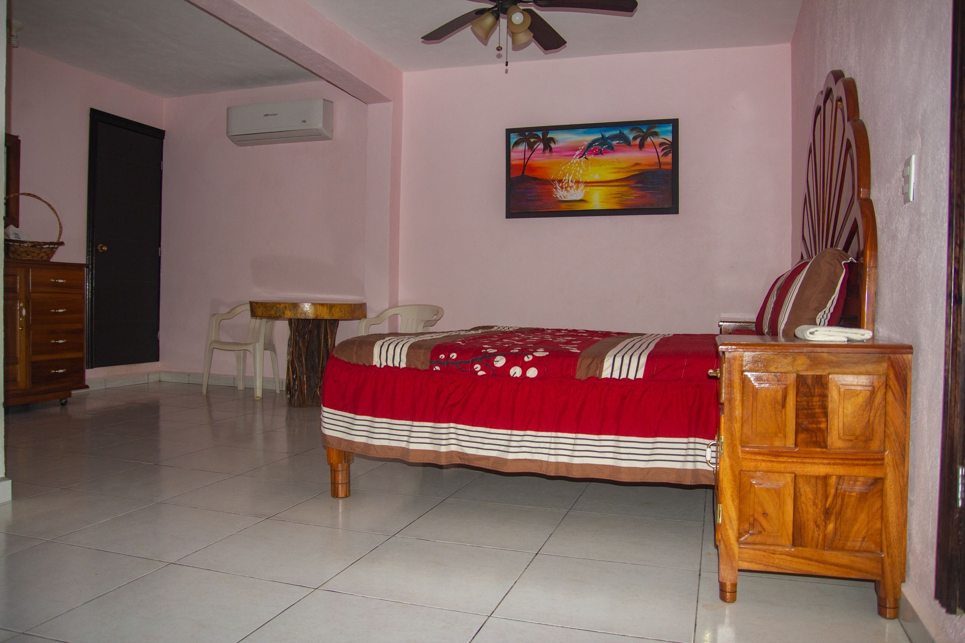 A bedroom with a red bed and a painting on the wall