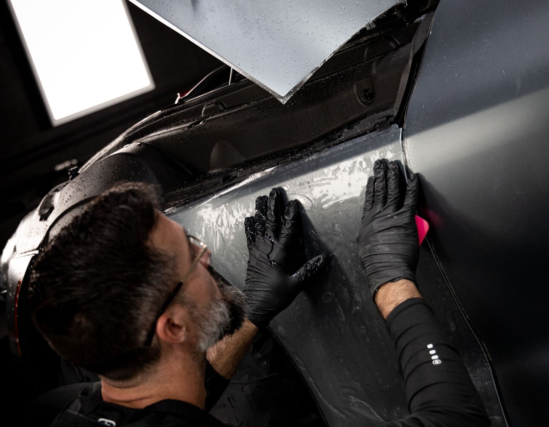 A man wearing gloves is working on a car in a garage.