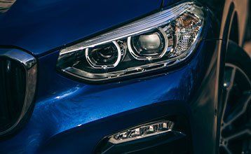 A close up of the headlight of a blue bmw x3.
