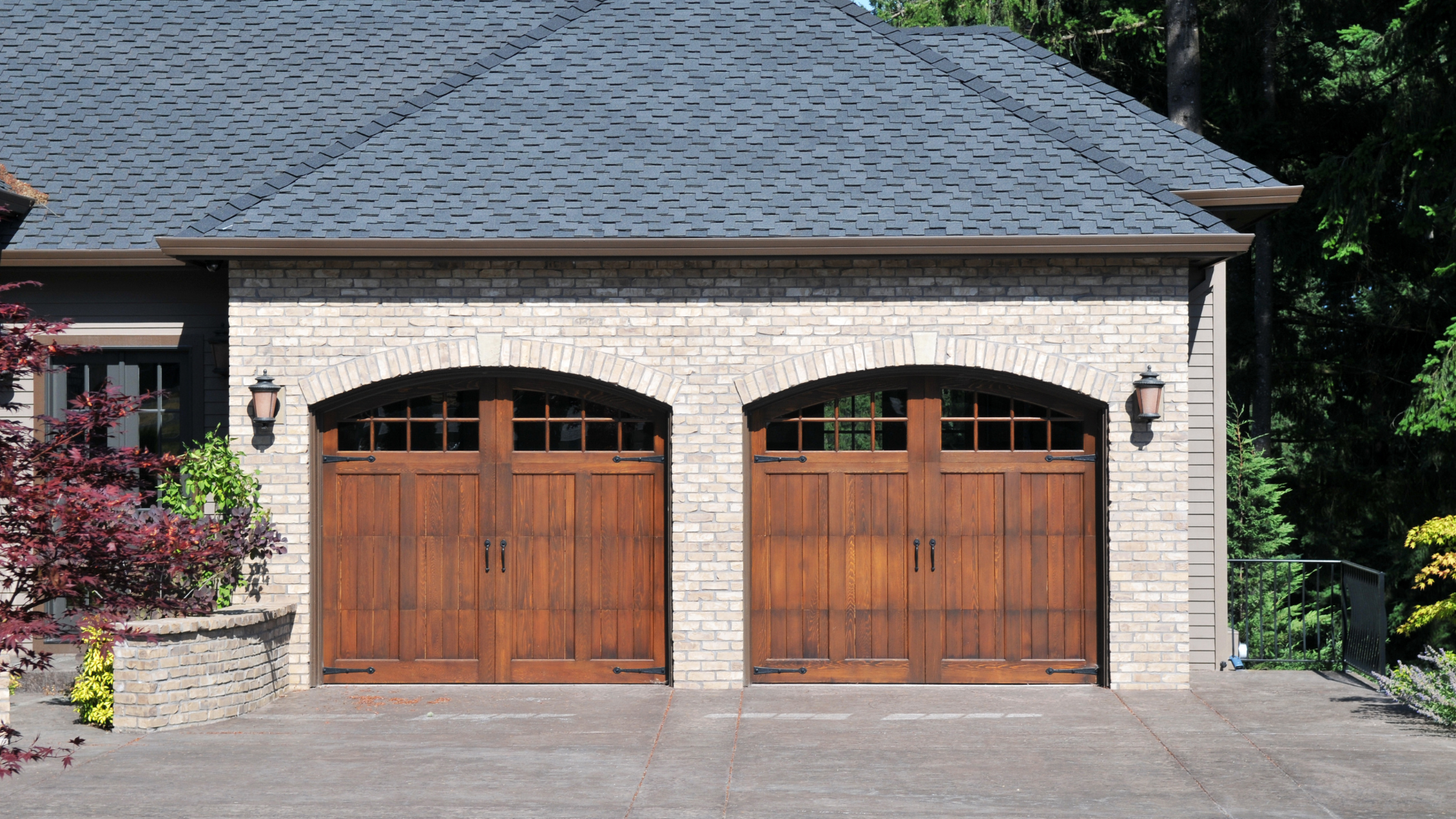 Two wooden garage doors with arched tops, set in a light brick facade, under a dark blue-gray roof.