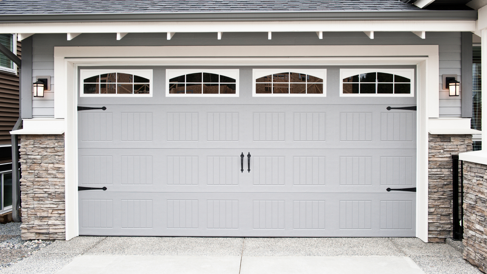 Gray garage door with arched window panels, black hardware, and stone accents.