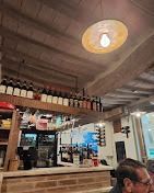 Interno del ristorante: bottiglie sugli scaffali, bancone del bar, luce dall'alto, soffitto in legno e una persona in primo piano.