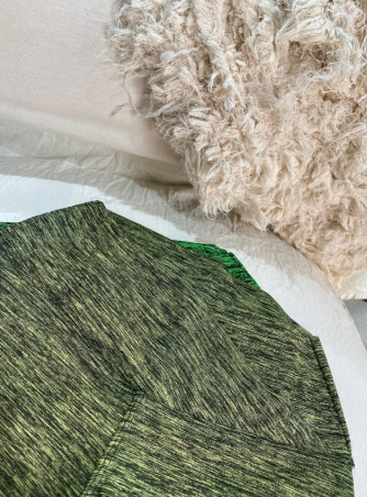 Un suéter verde está sentado sobre una cama al lado de una almohada blanca.