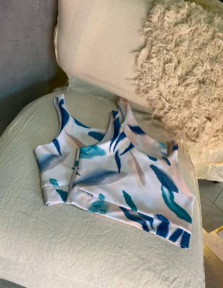 Un top corto blanco y azul está sobre una silla al lado de una almohada.