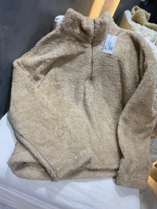 Un suéter de osito de peluche de color marrón está sobre una mesa blanca.