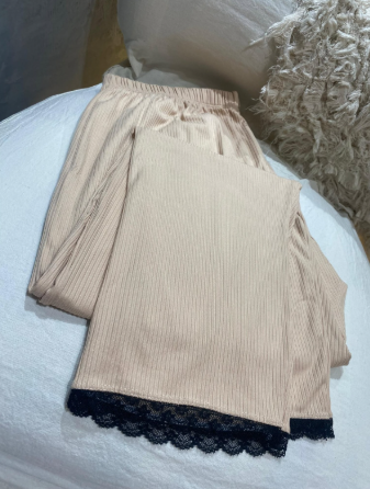 Un par de pantalones con ribete de encaje negro están sobre una cama.