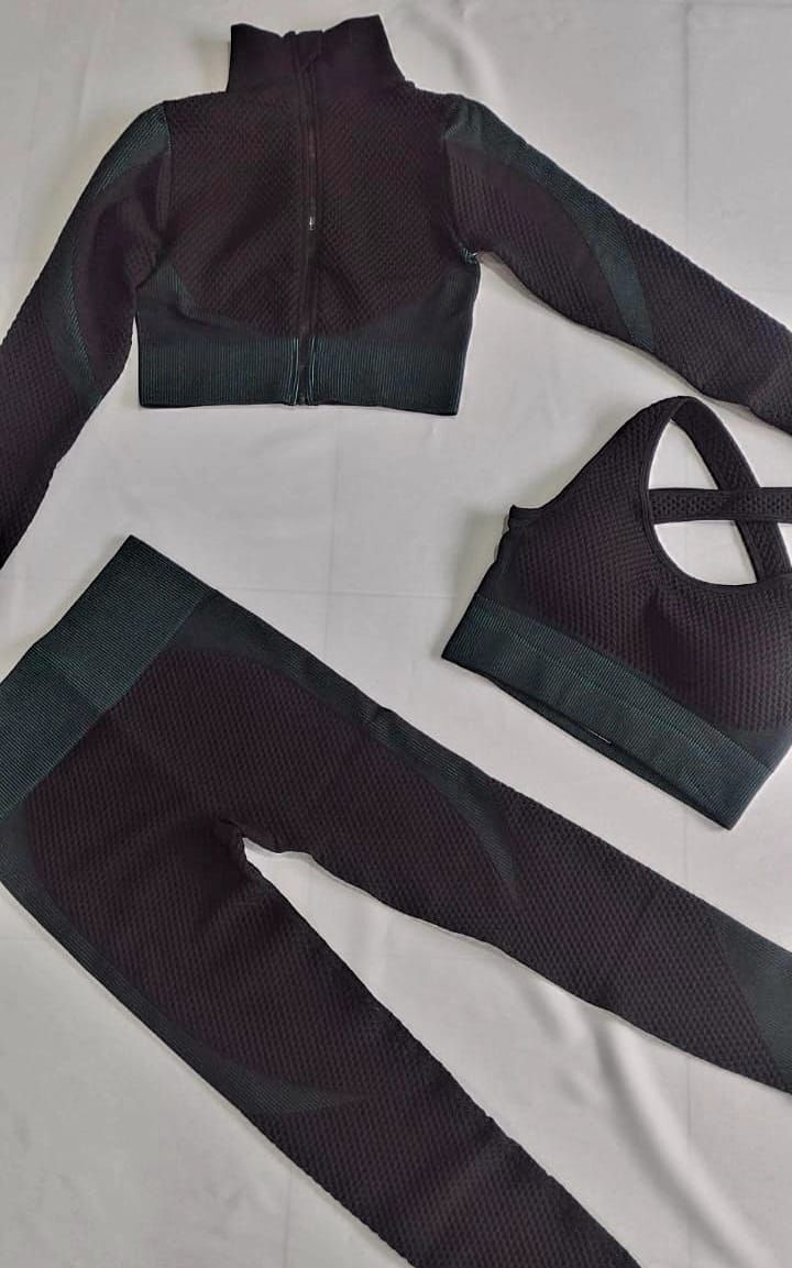 Conjunto de entrenamiento negro: chaqueta, sujetador deportivo y mallas sobre una superficie blanca.