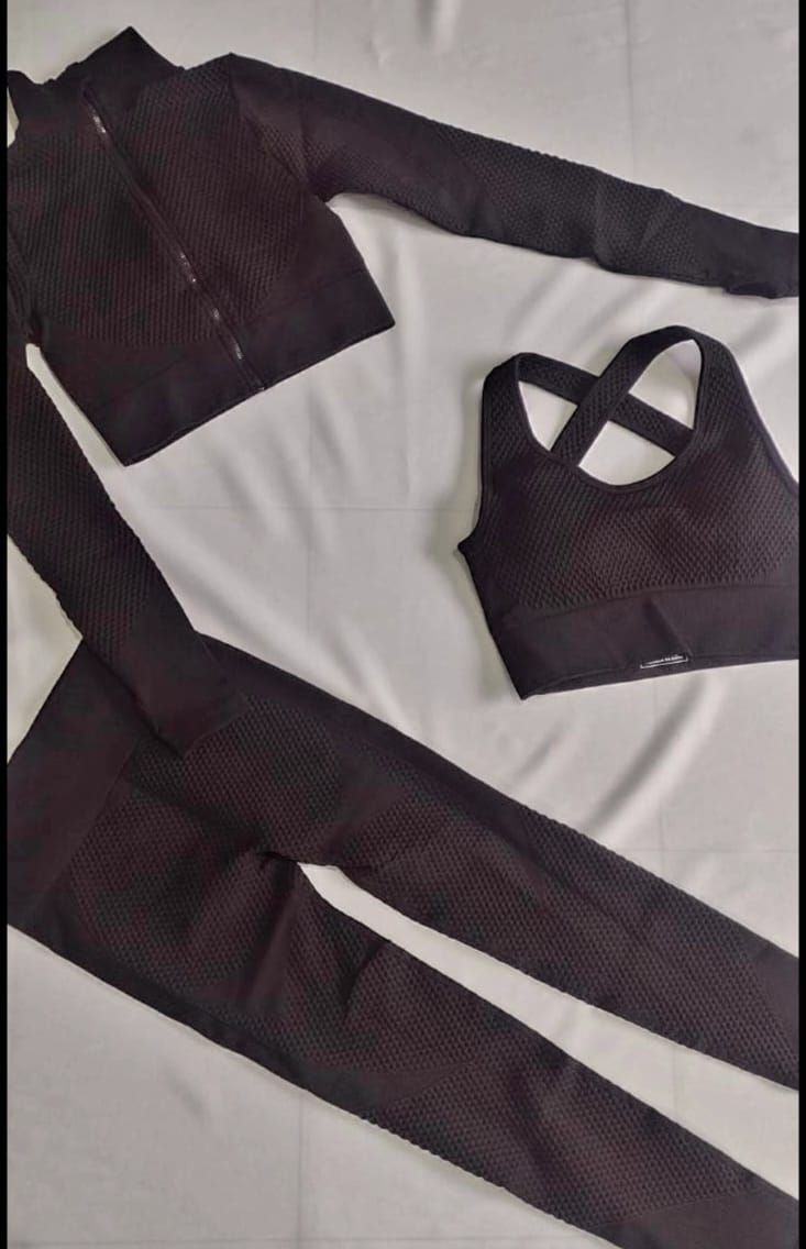 Conjunto de entrenamiento negro: chaqueta, sujetador deportivo y mallas sobre una superficie blanca.