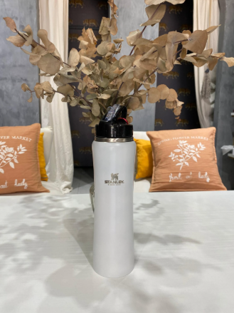 Una botella de agua blanca está sobre una mesa con flores dentro.