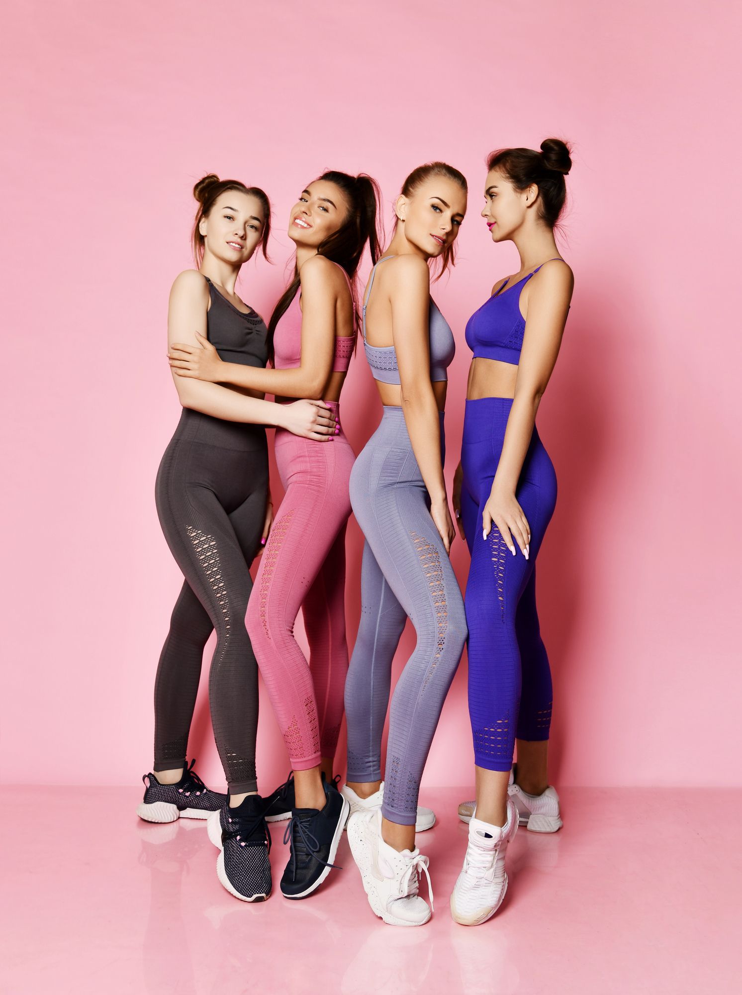Cuatro mujeres vestidas con ropa deportiva posan para una fotografía sobre un fondo rosa.