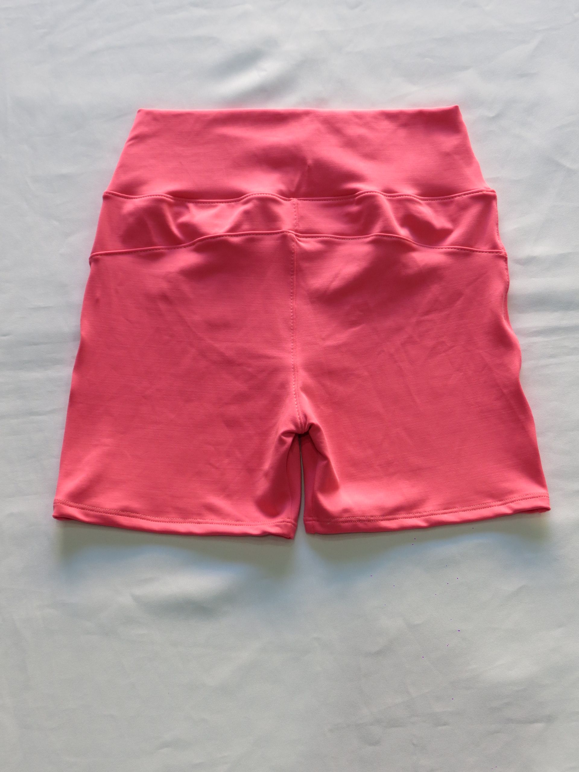 Pantalones cortos de ciclista de cintura alta de color rosa sobre una superficie blanca.