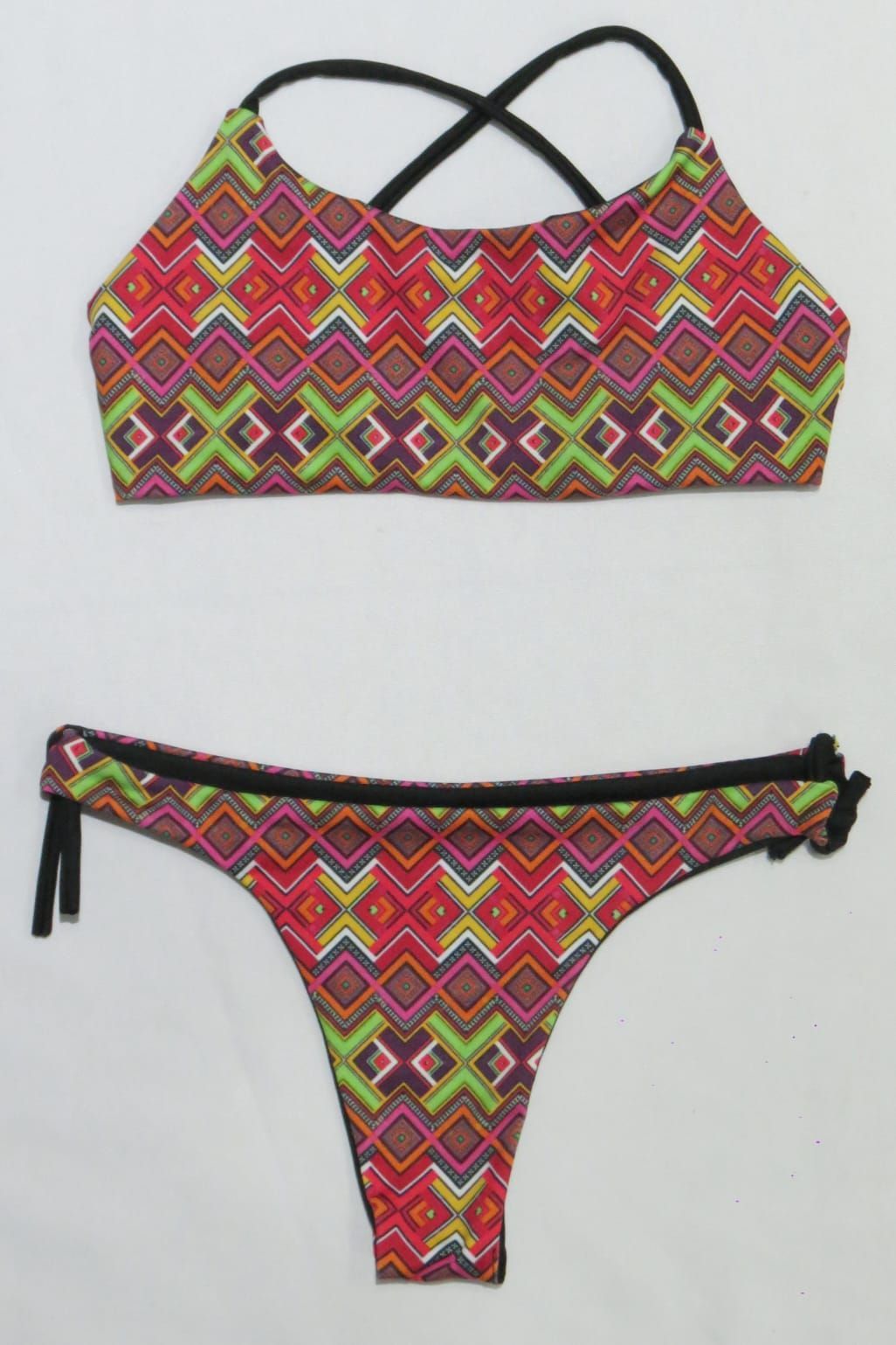 Conjunto de bikini de dos piezas con estampado geométrico en tonos rojo, rosa y verde, tirantes y ribete en color negro.