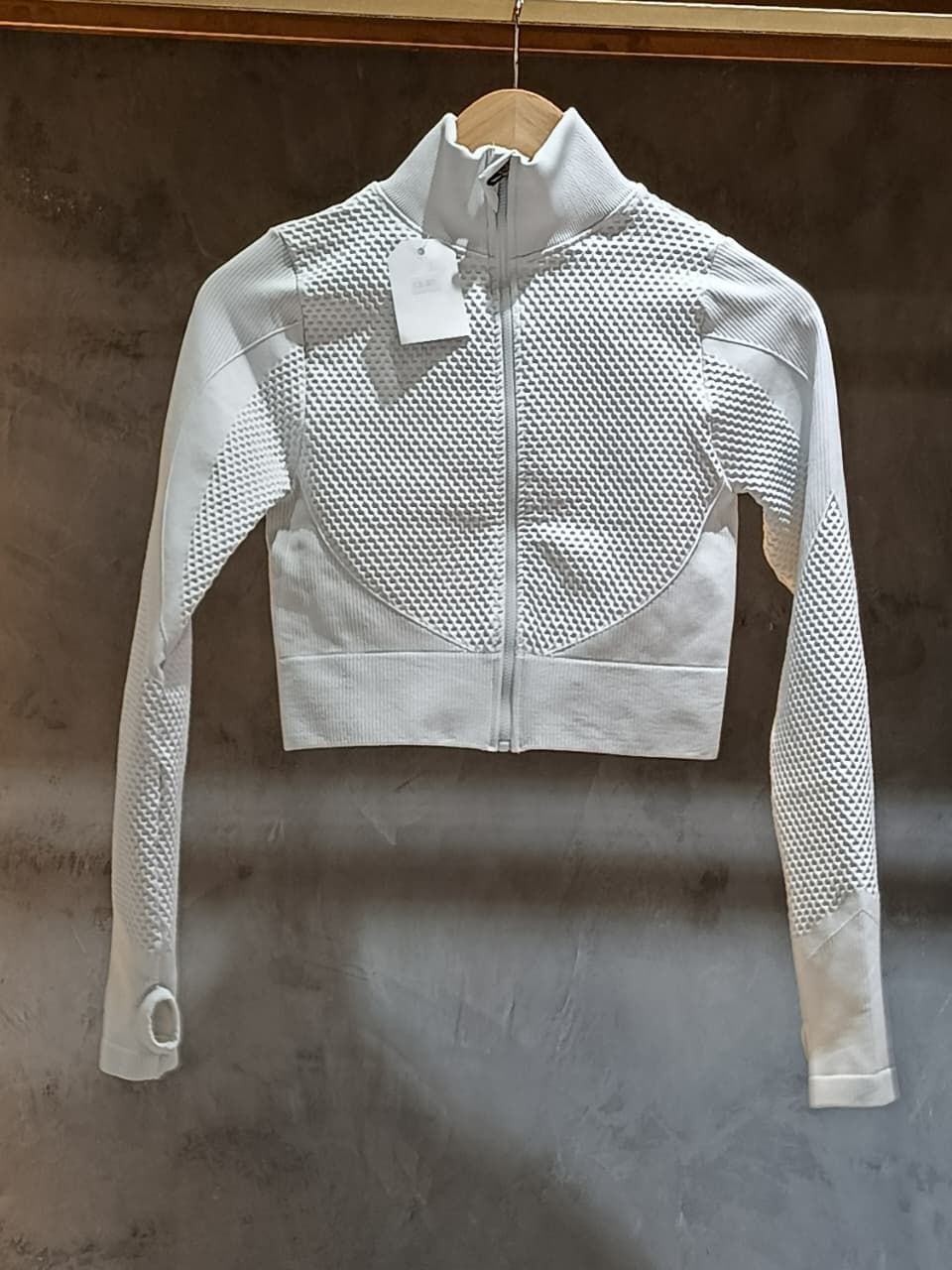 Chaqueta deportiva corta blanca con patrón perforado, cierre de cremallera y orificios para los pulgares.