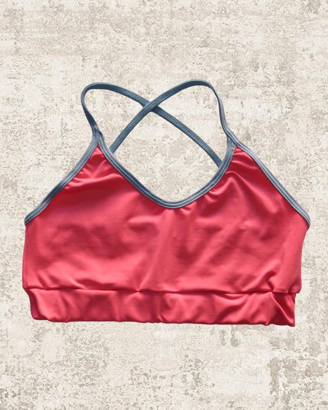 Sujetador deportivo rosa con ribete gris y tirantes cruzados.