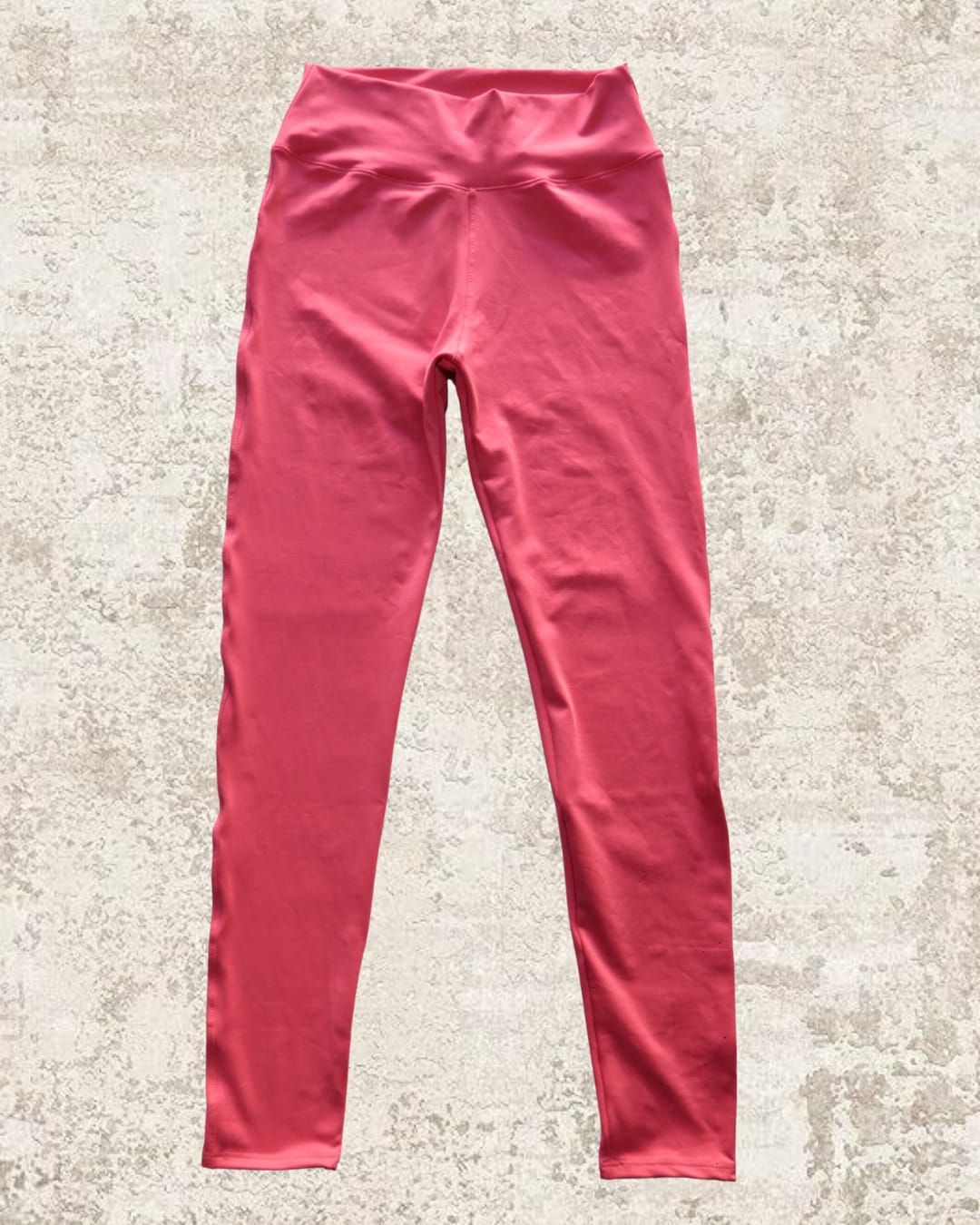 Leggings de cintura alta de color rosa sobre un fondo de textura neutra.