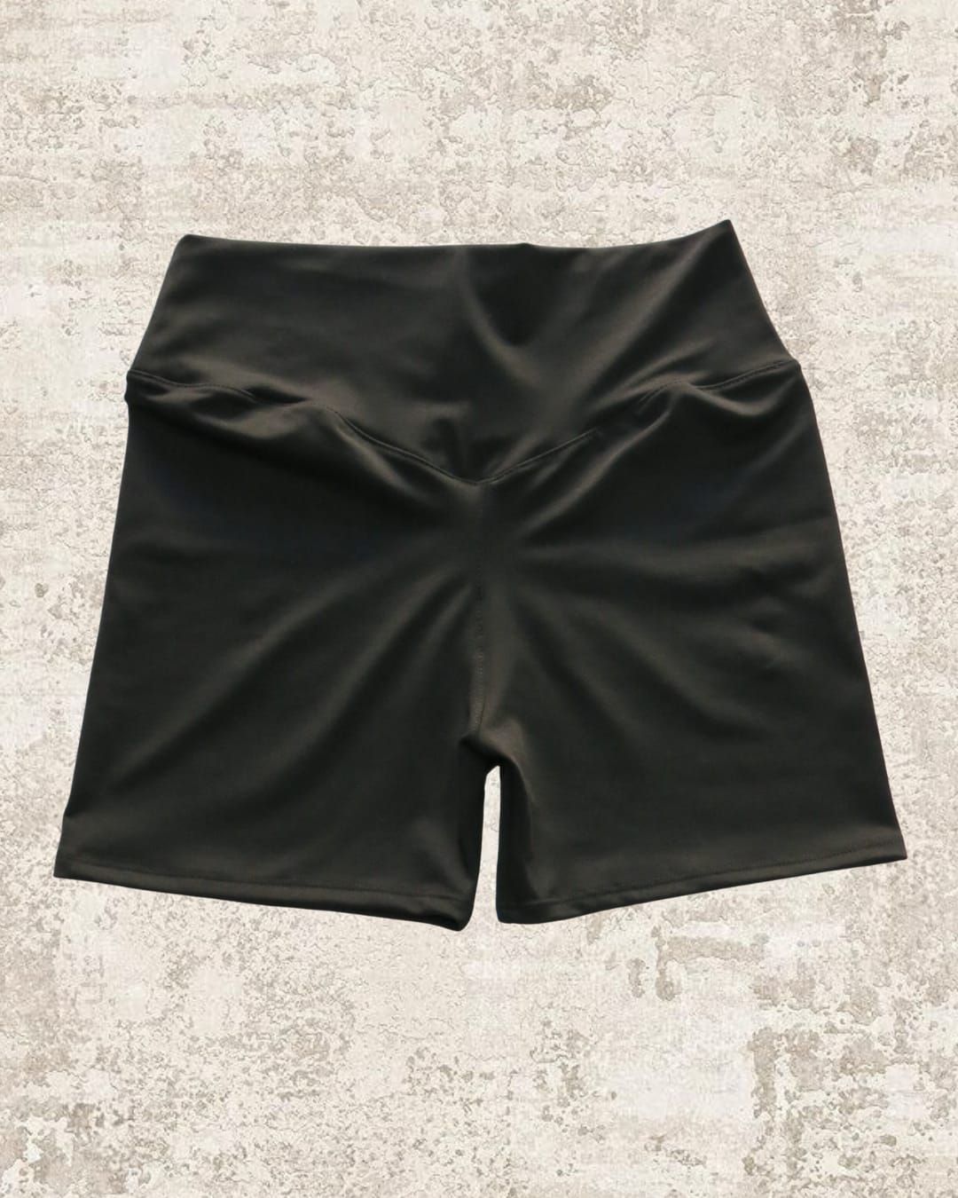 Pantalones cortos deportivos negros de cintura alta sobre una superficie texturizada de color claro.