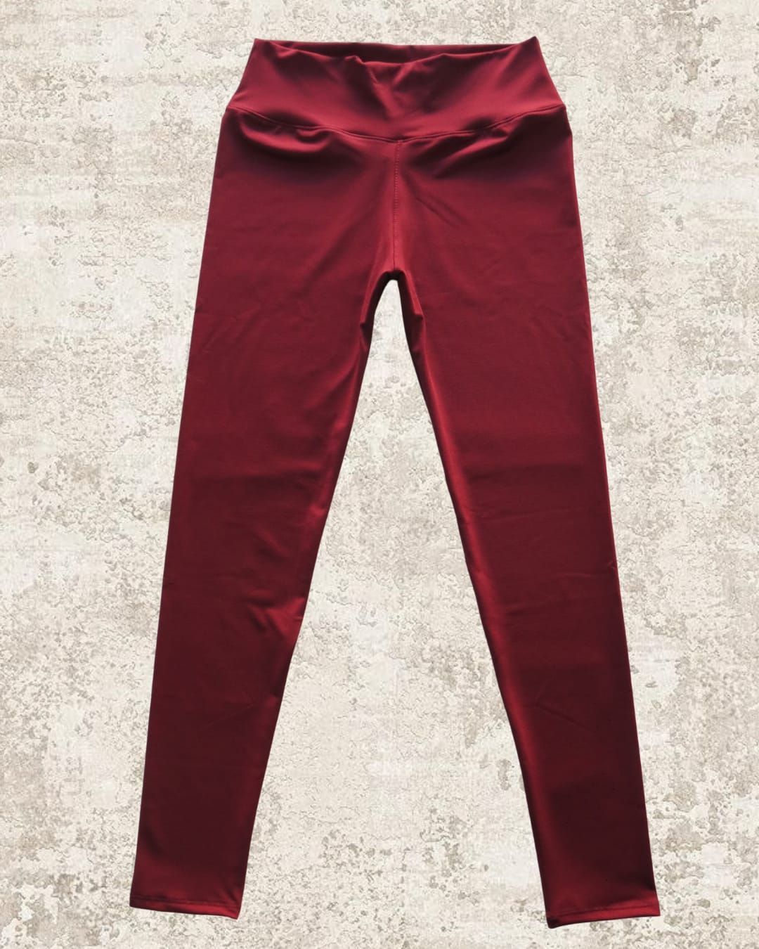 Leggings de cintura alta de color burdeos expuestos sobre una superficie texturizada de color marrón claro.