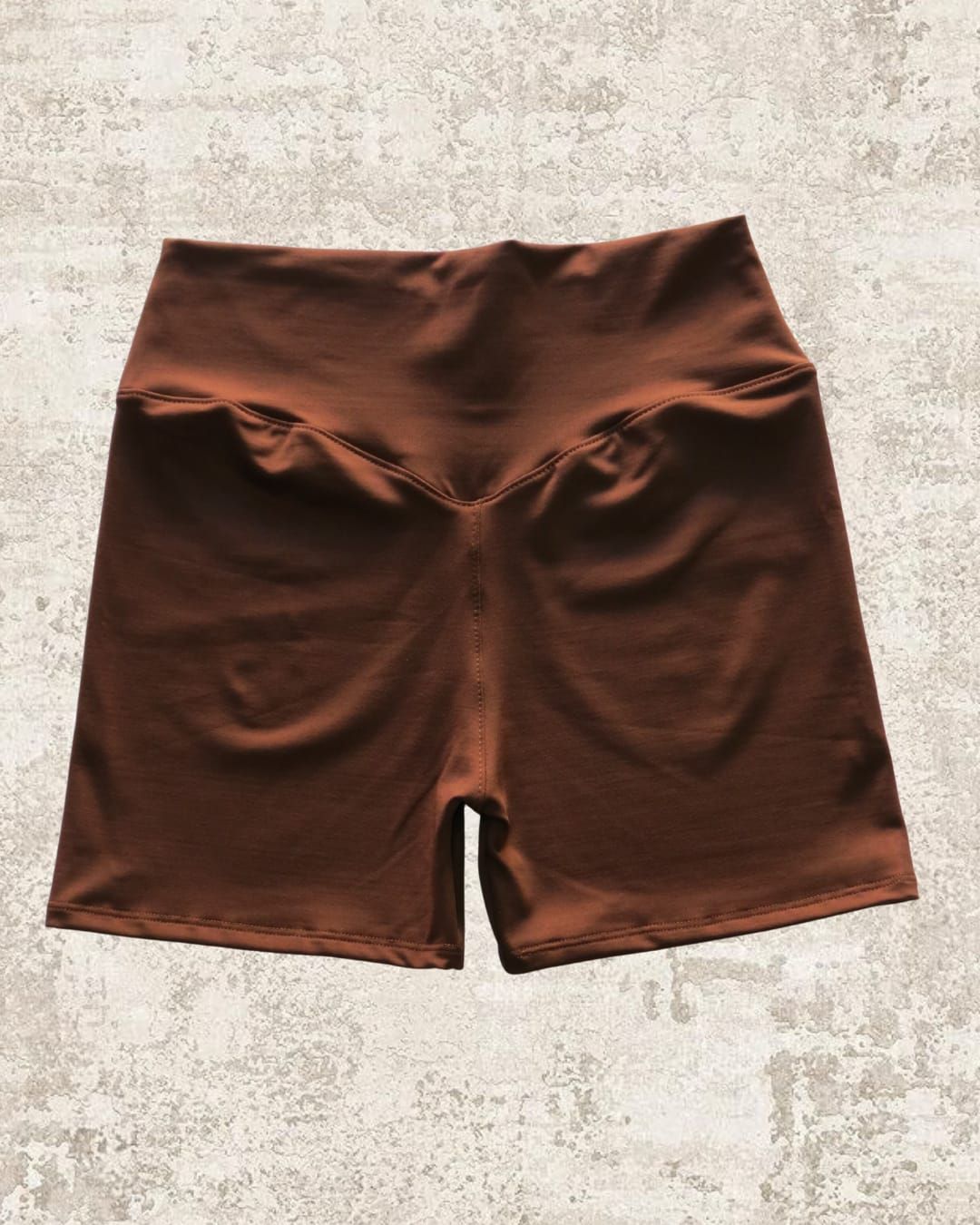 Pantalones cortos de ciclista de cintura alta de color marrón sobre una superficie texturizada de color claro.