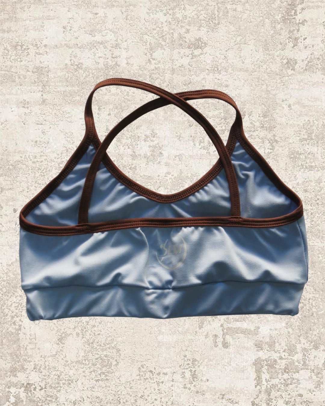 Sujetador deportivo de color azul con ribetes y tirantes marrones sobre fondo texturizado.