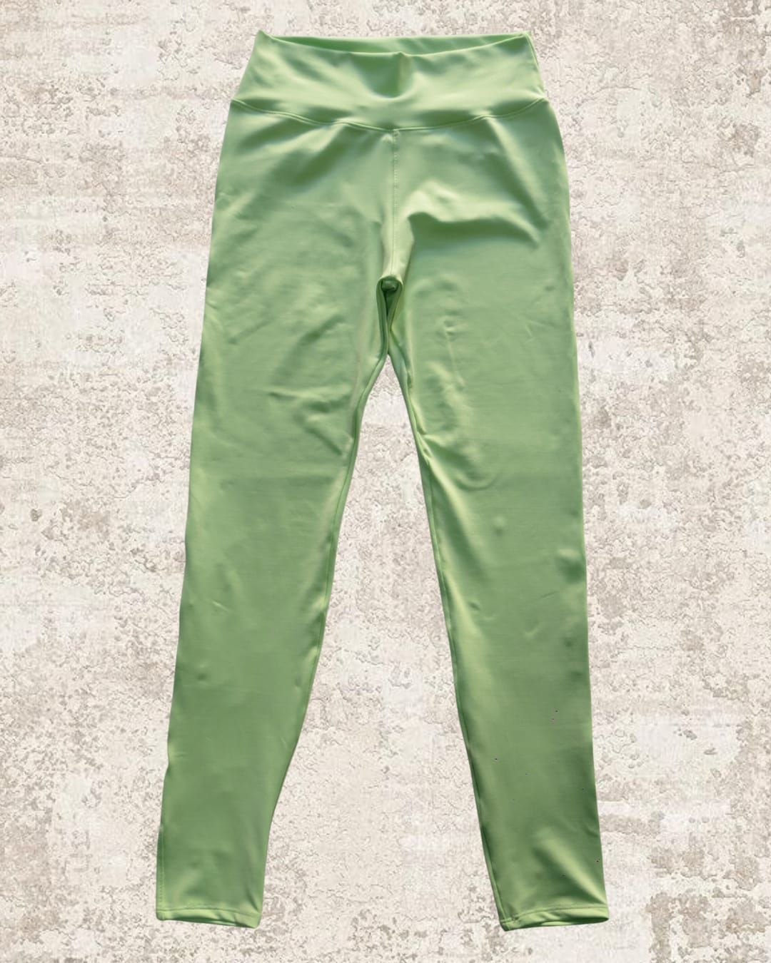Leggings de color verde claro sobre una superficie texturizada de color marrón claro.