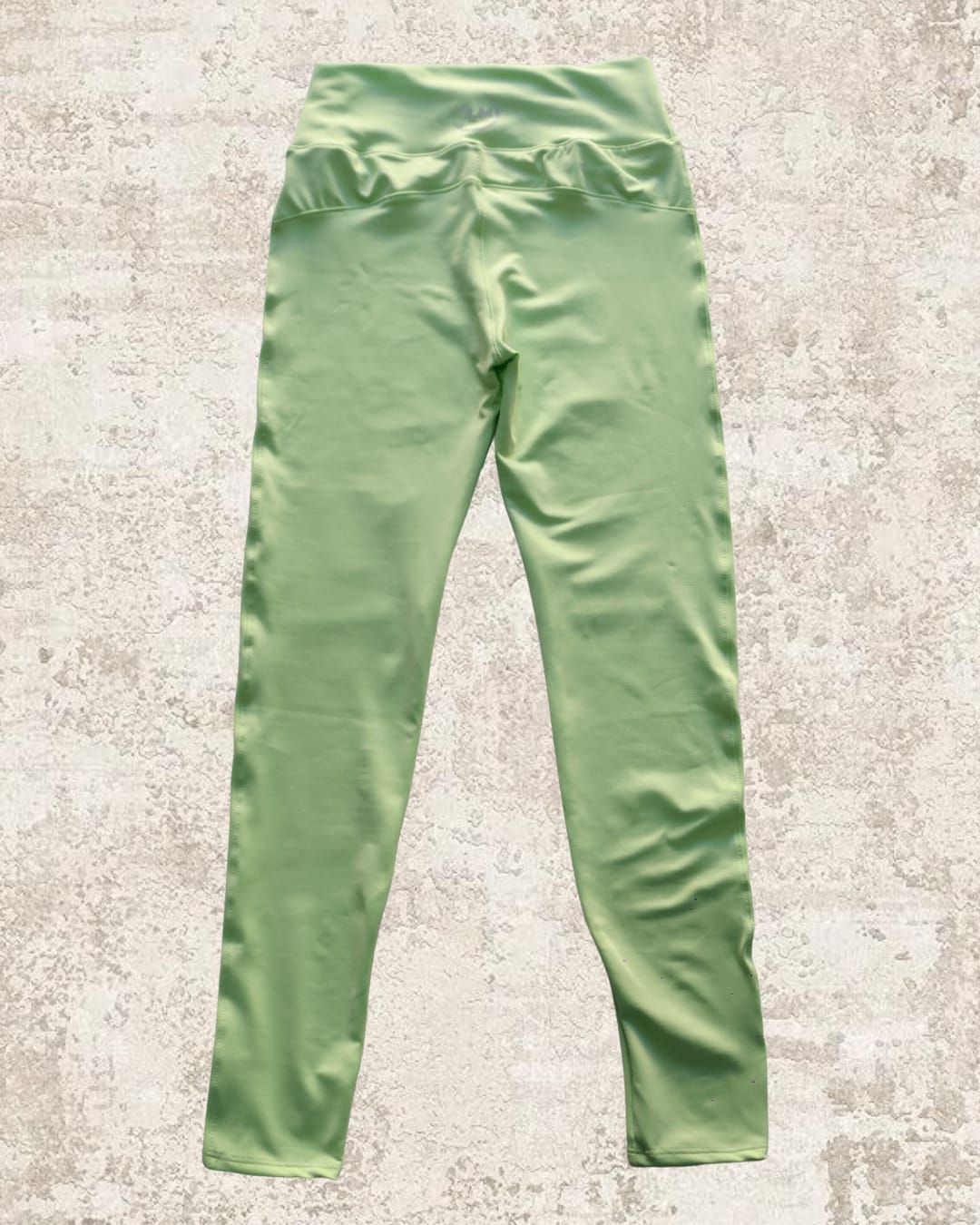 Leggings verde claro sobre una superficie texturizada en tonos neutros.
