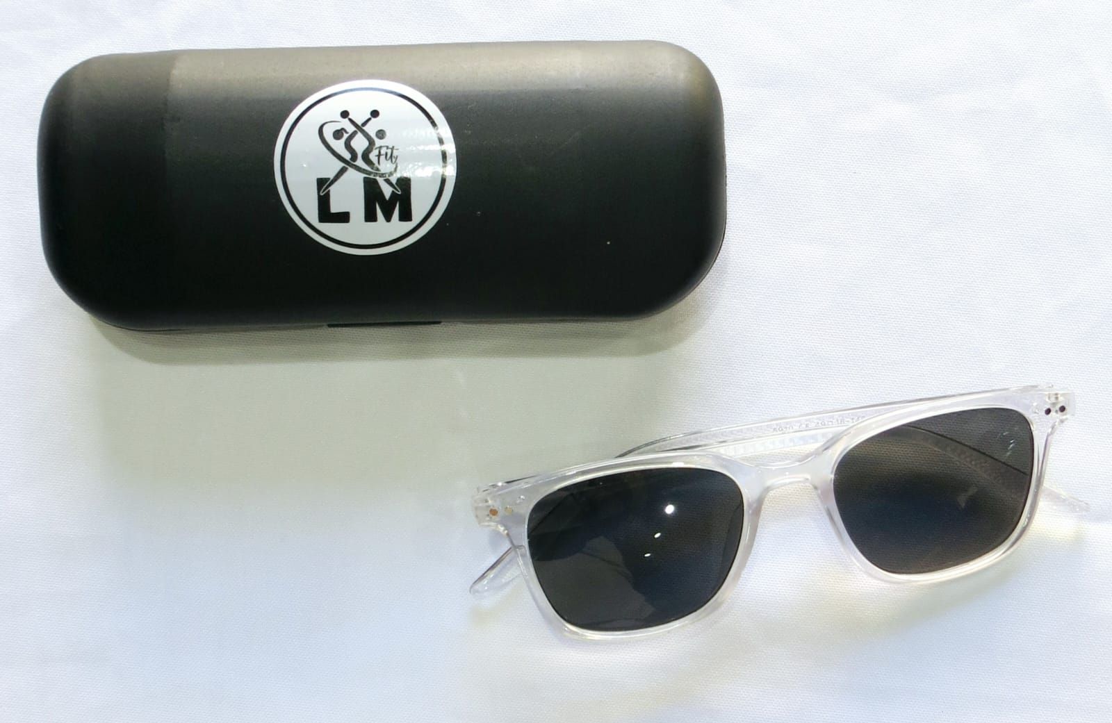 Gafas de sol con montura transparente y lentes negras junto a un estuche negro con logotipo.