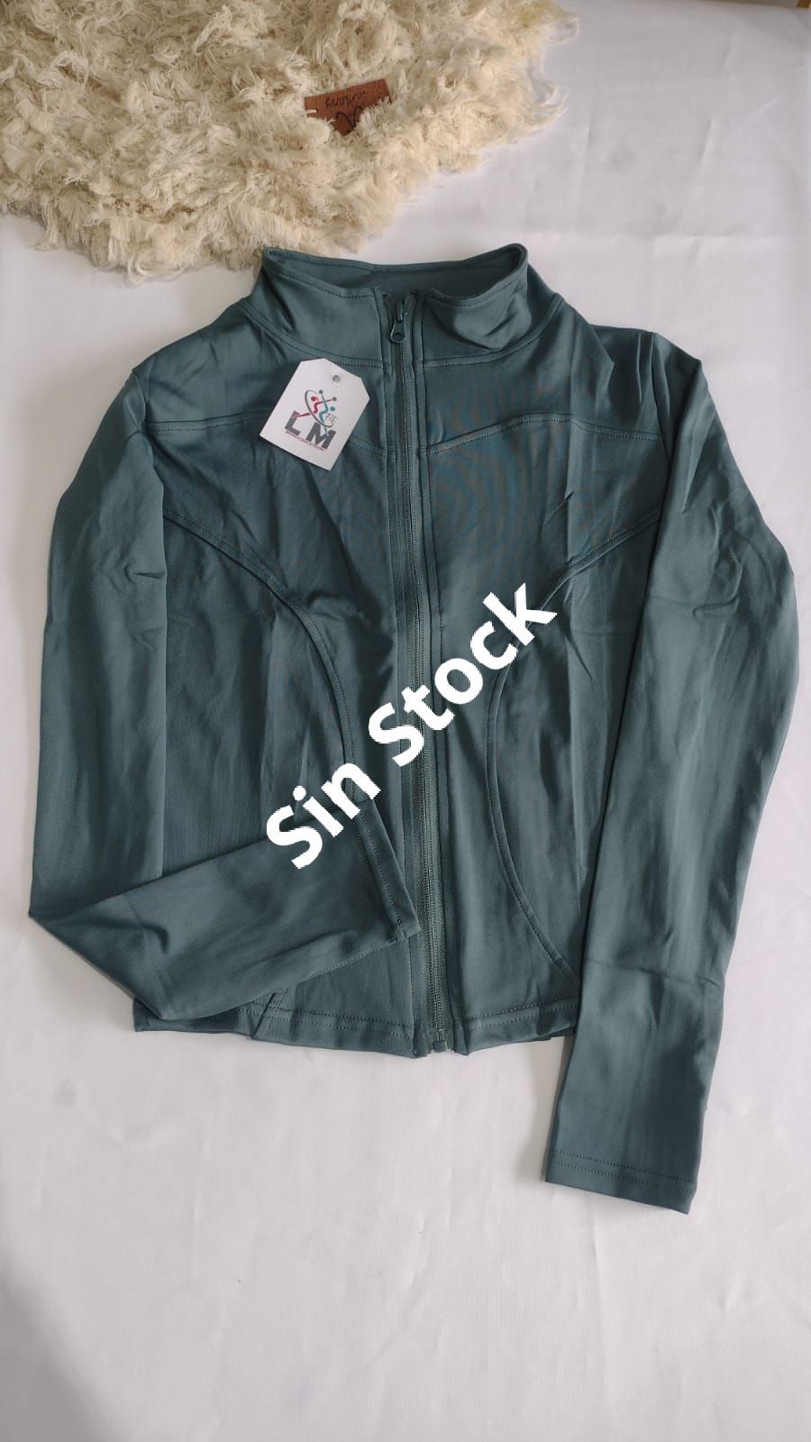 Chaqueta deportiva color verde azulado con cremallera, doblada sobre una superficie blanca con una etiqueta con precio.