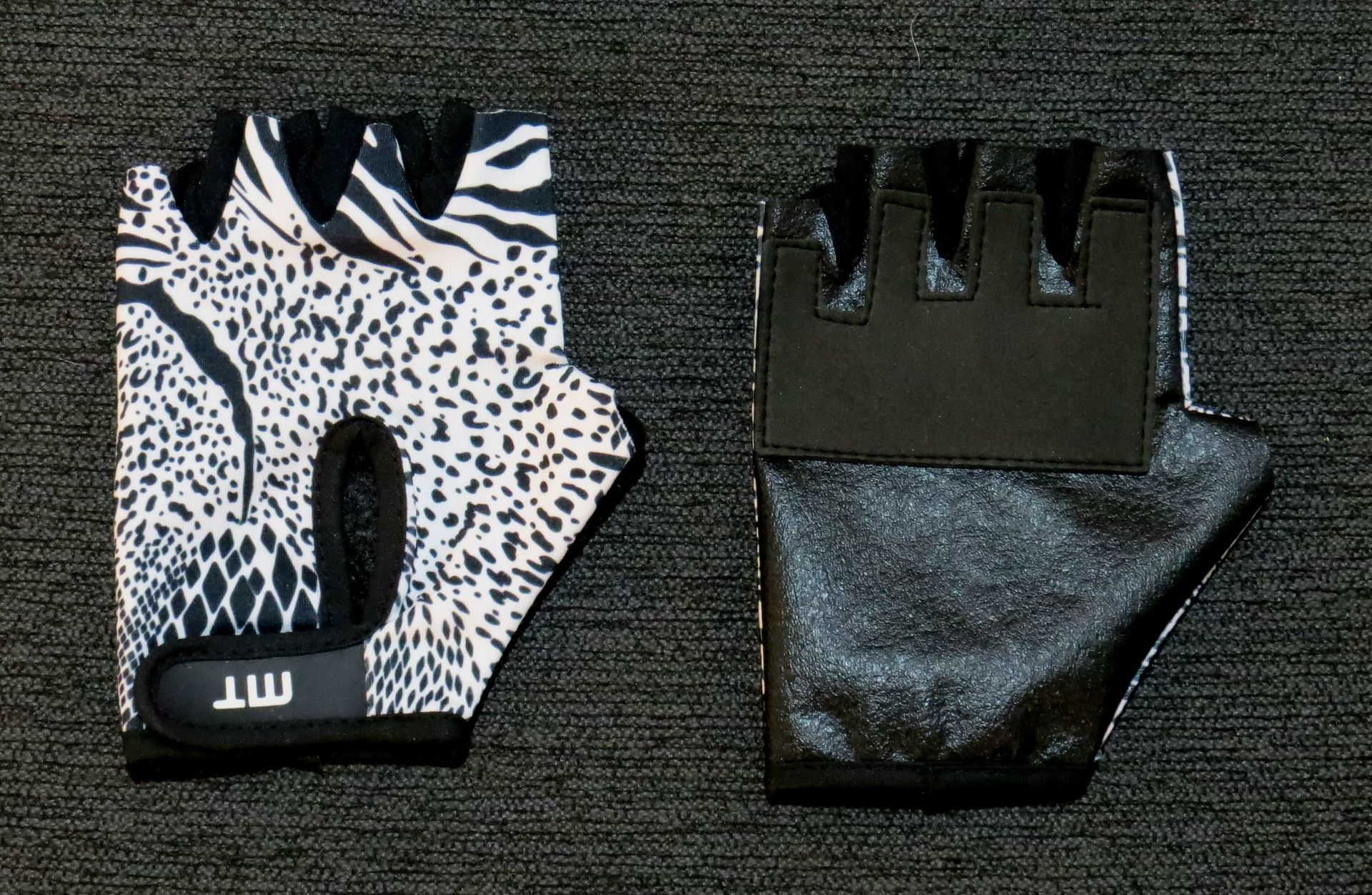 Guantes de ciclismo sin dedos con diseño de estampado animal en blanco y negro, sobre una superficie oscura.