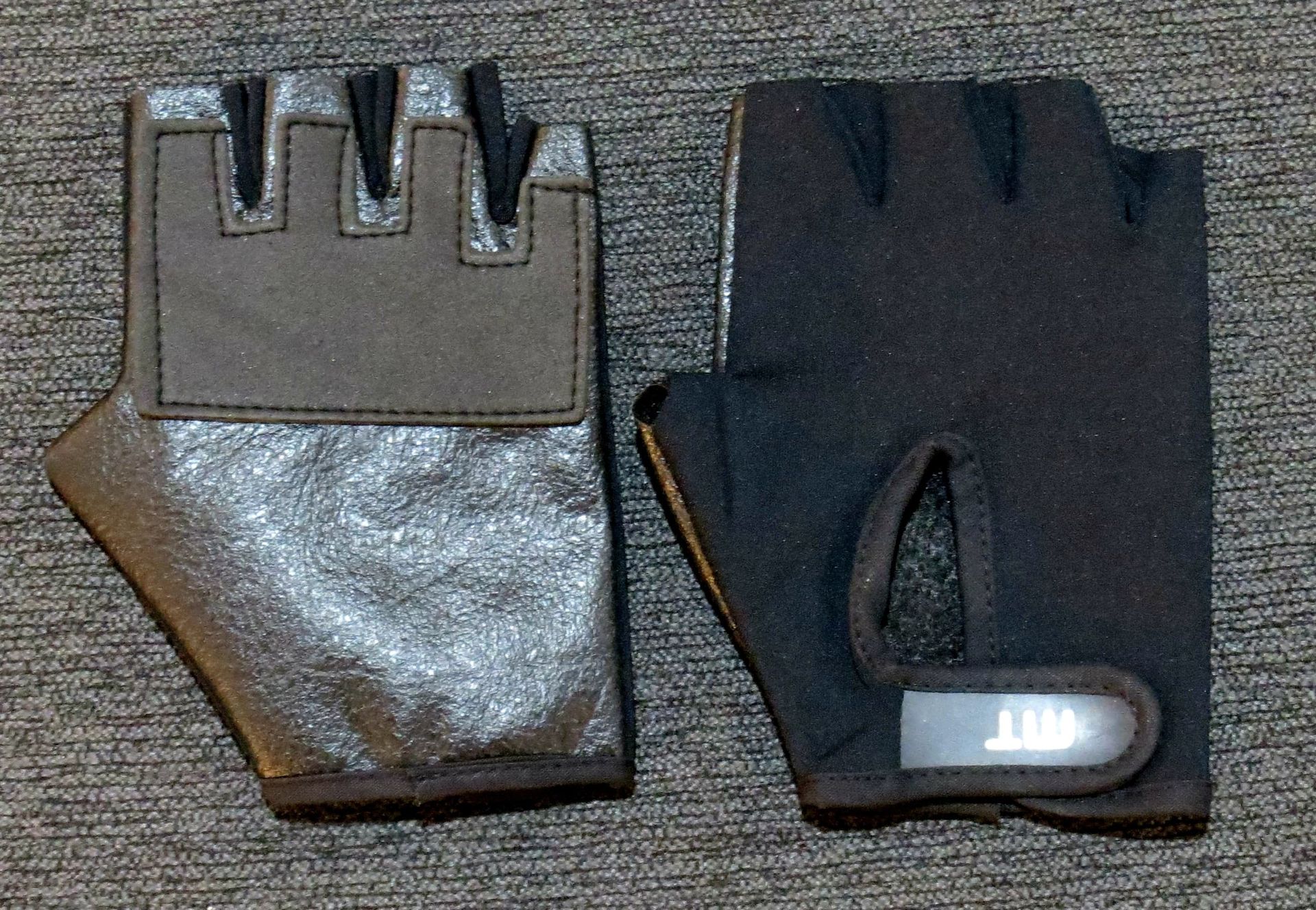 Par de guantes de entrenamiento sin dedos de color negro y plateado, palma hacia arriba y palma hacia abajo.