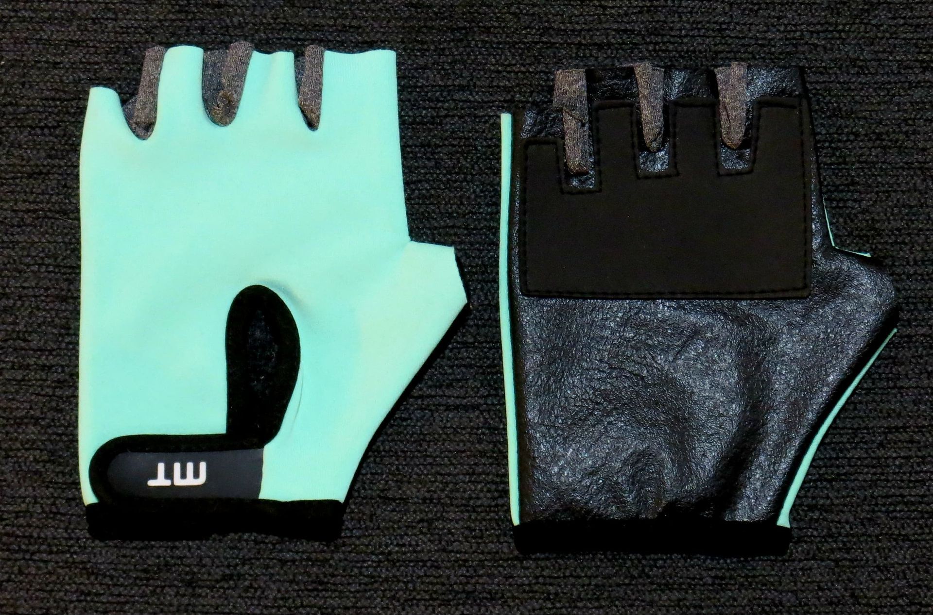 Guantes de ciclismo de color verde menta con detalles en negro y palma acolchada, colocados sobre una superficie oscura.