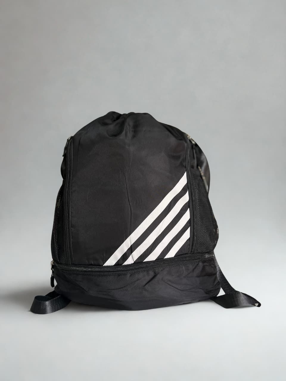 Mochila Adidas negra con cordón y rayas blancas.
