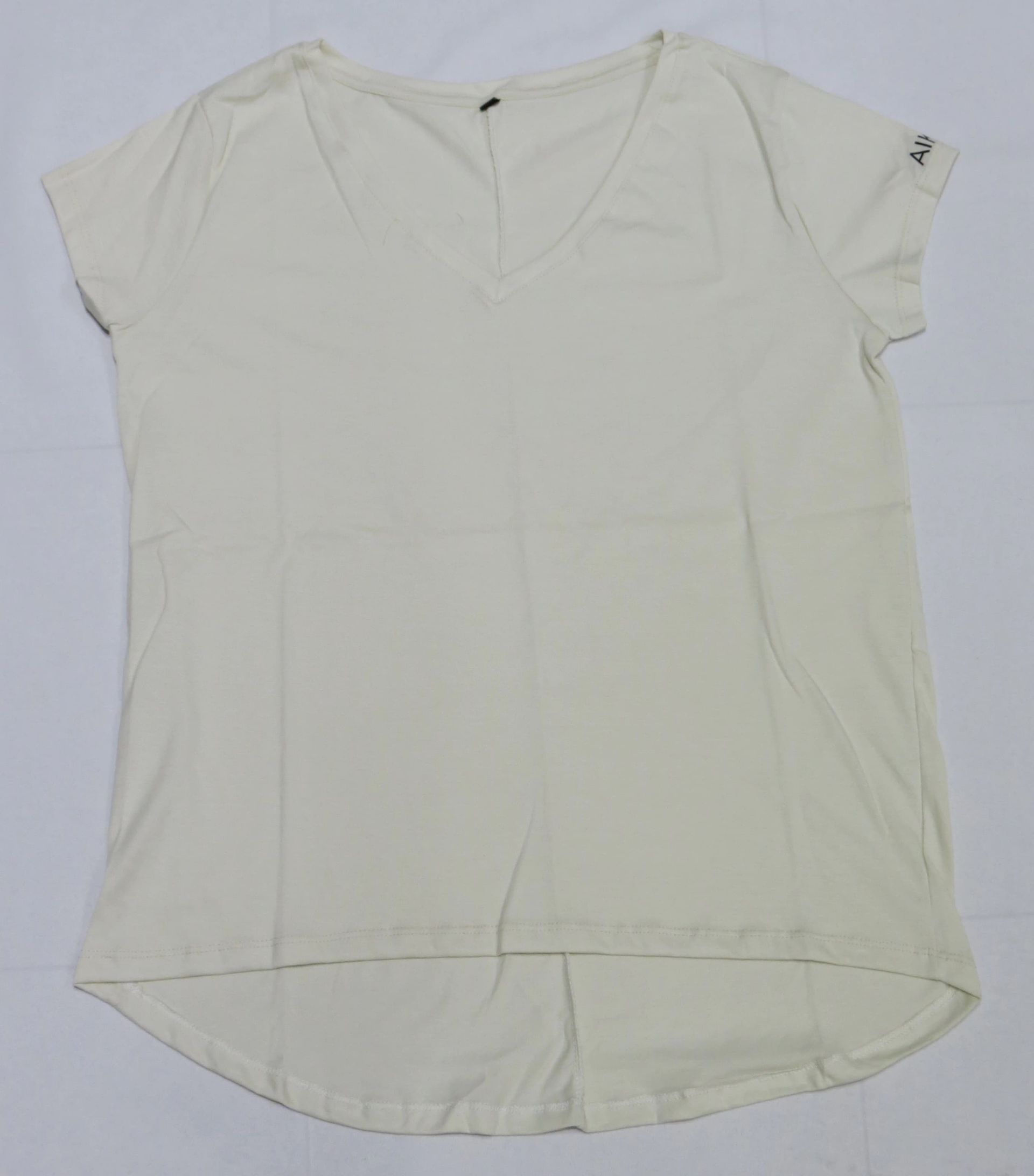 Camiseta de color crema con cuello en V, mangas cortas y bajo redondeado, colocada plana sobre una superficie blanca.