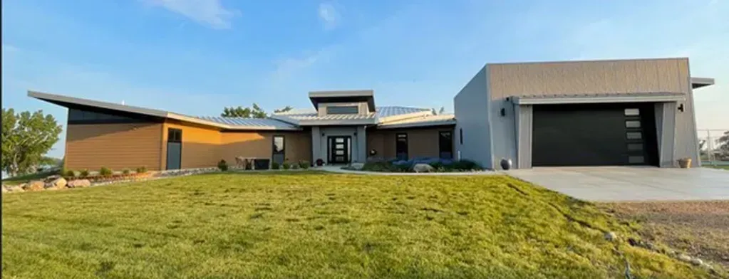 Modern, single-story house with a flat roof and attached garage; set in a grassy yard under a blue sky.