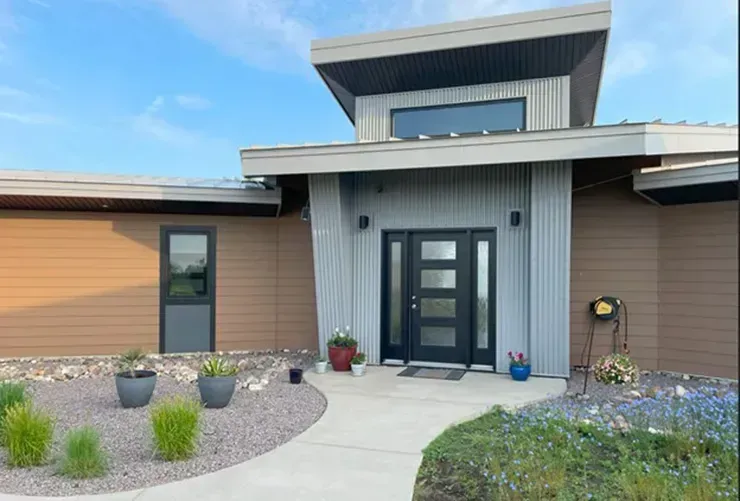 Modern home exterior with brown and gray siding, black door, and landscaped yard.