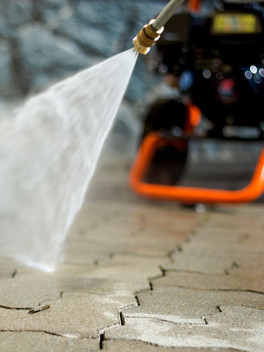 a person is using a high pressure washer to clean a sidewalk .