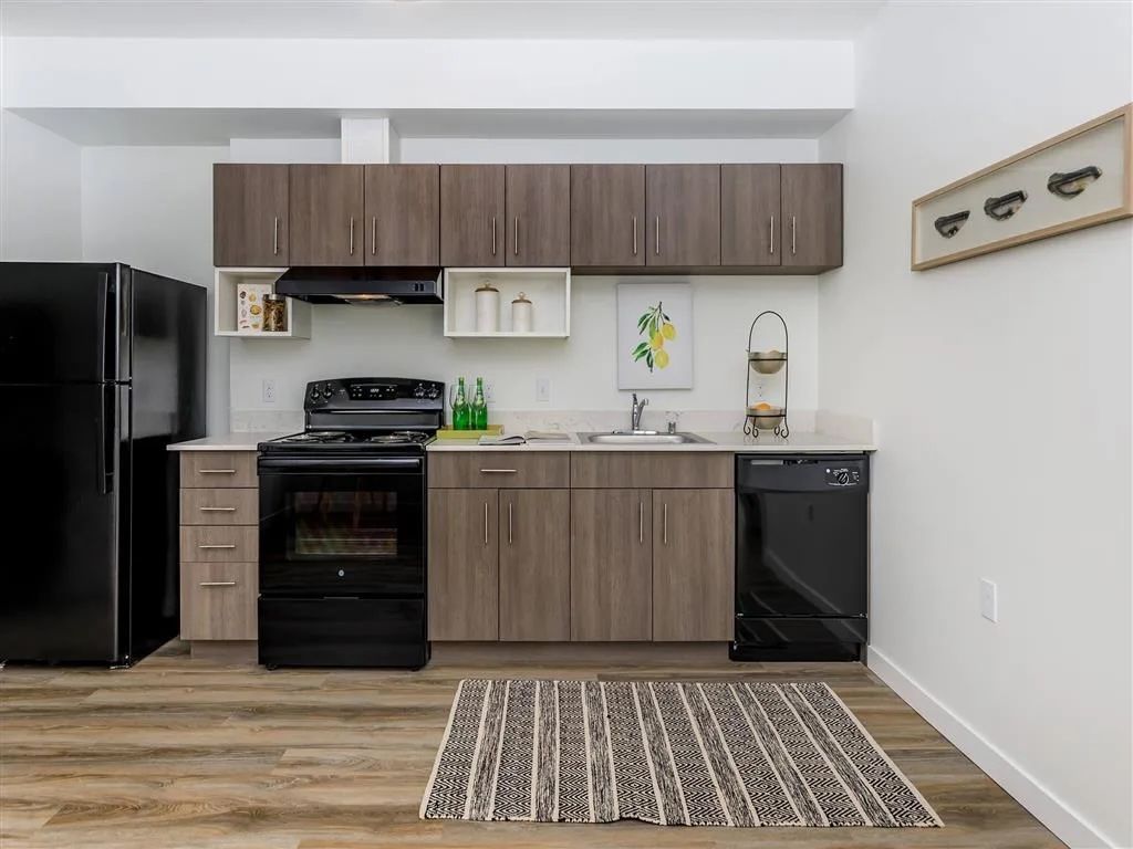 Kitchen with black appliances, brown cabinets, white countertop, and wood floor.