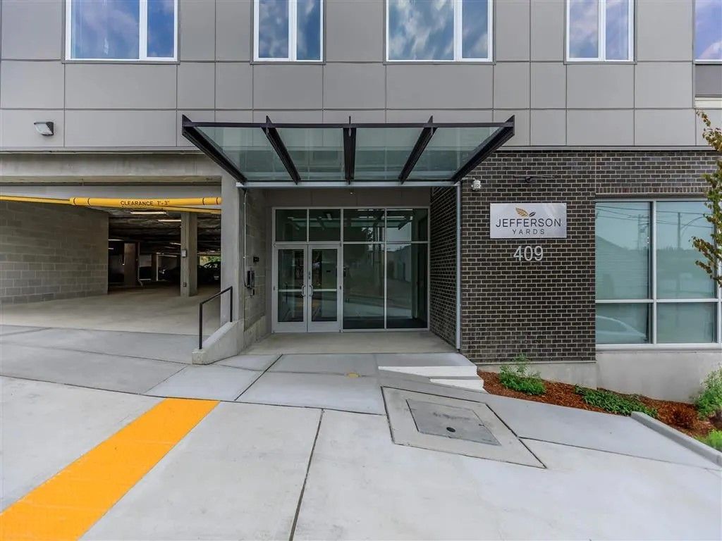 Entrance to an apartment building with glass doors, a canopy, and a parking garage on the left.